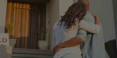Happy Scottsdale home buyers in front of the wooden front door of their new place with a SOLD sign in front of it.